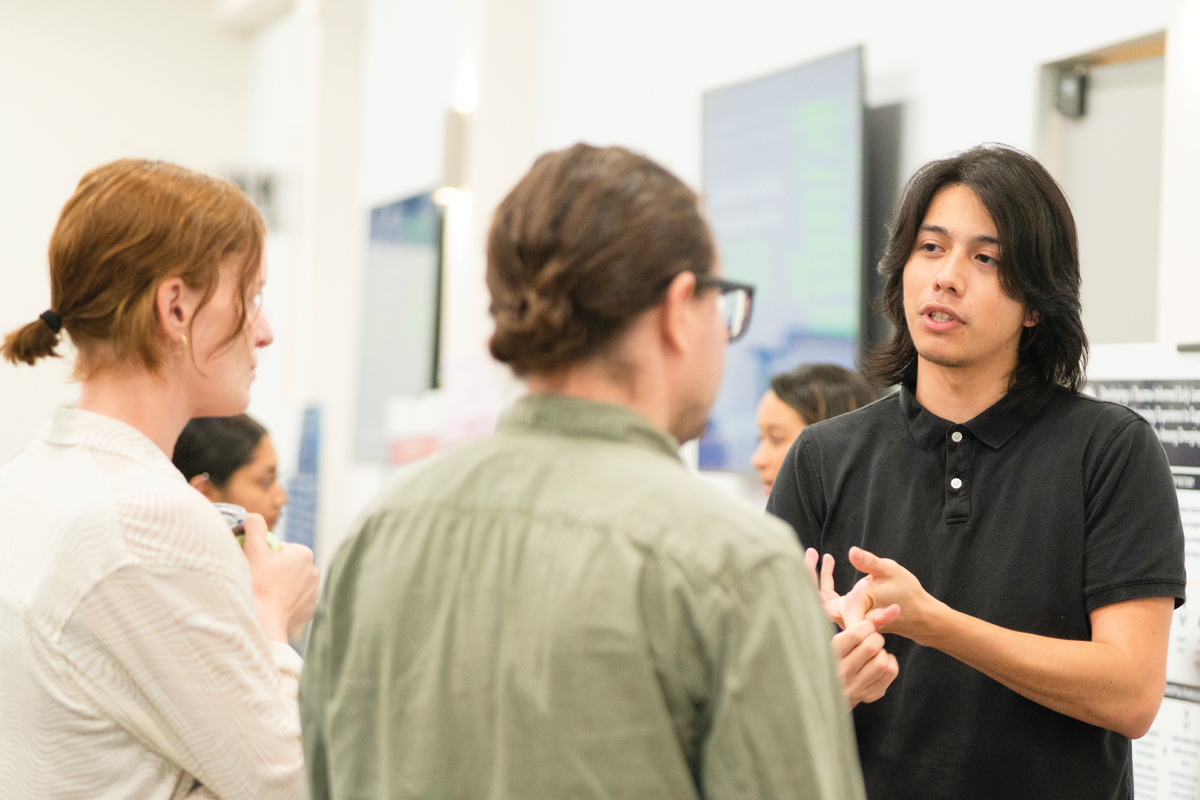 A Stanislaus State student gestures while talking with two other people during a campus gathering indoors.