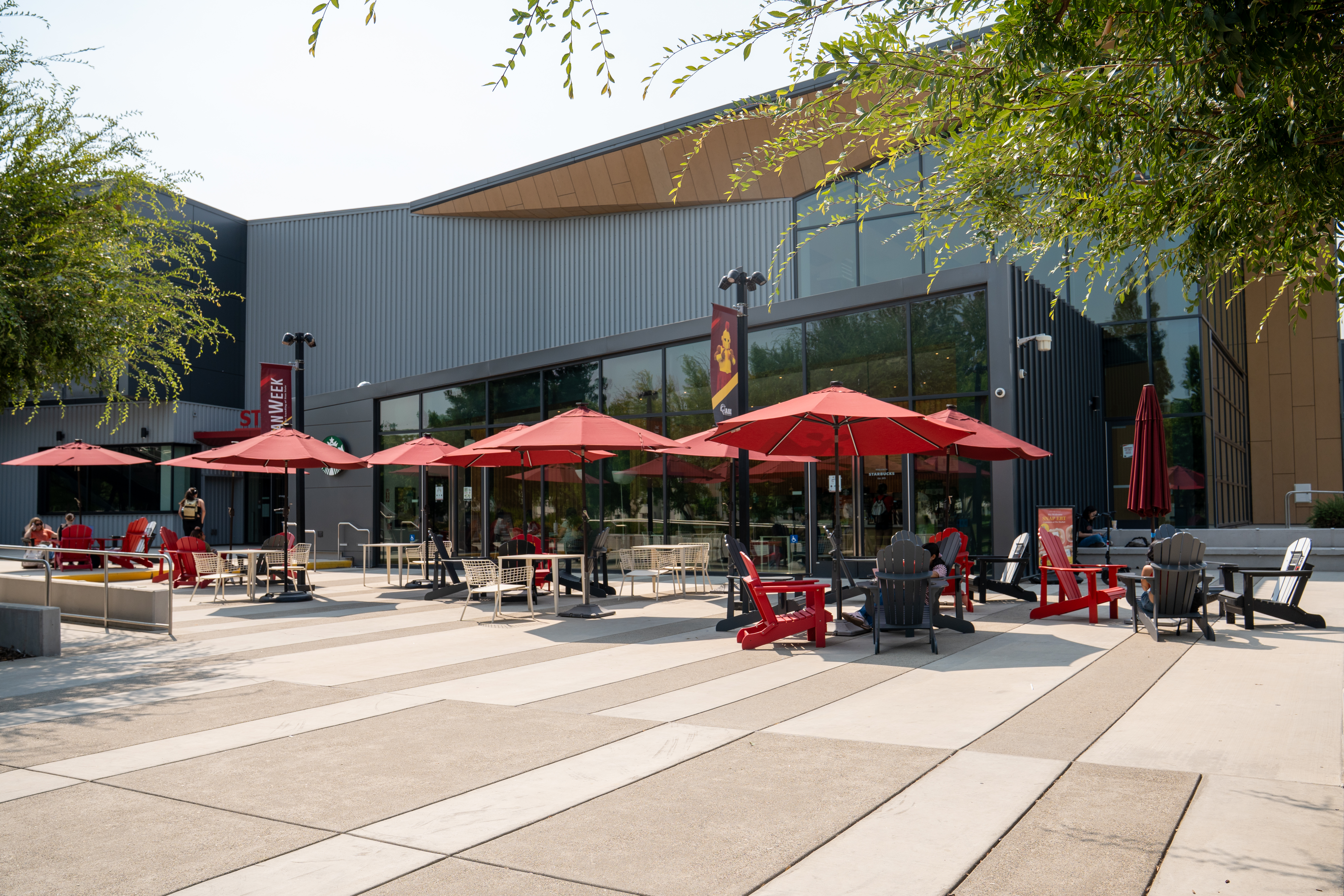 Outdoor patio seating with red umbrellas in Warrior Square outside the Stan State Student Center Starbucks.