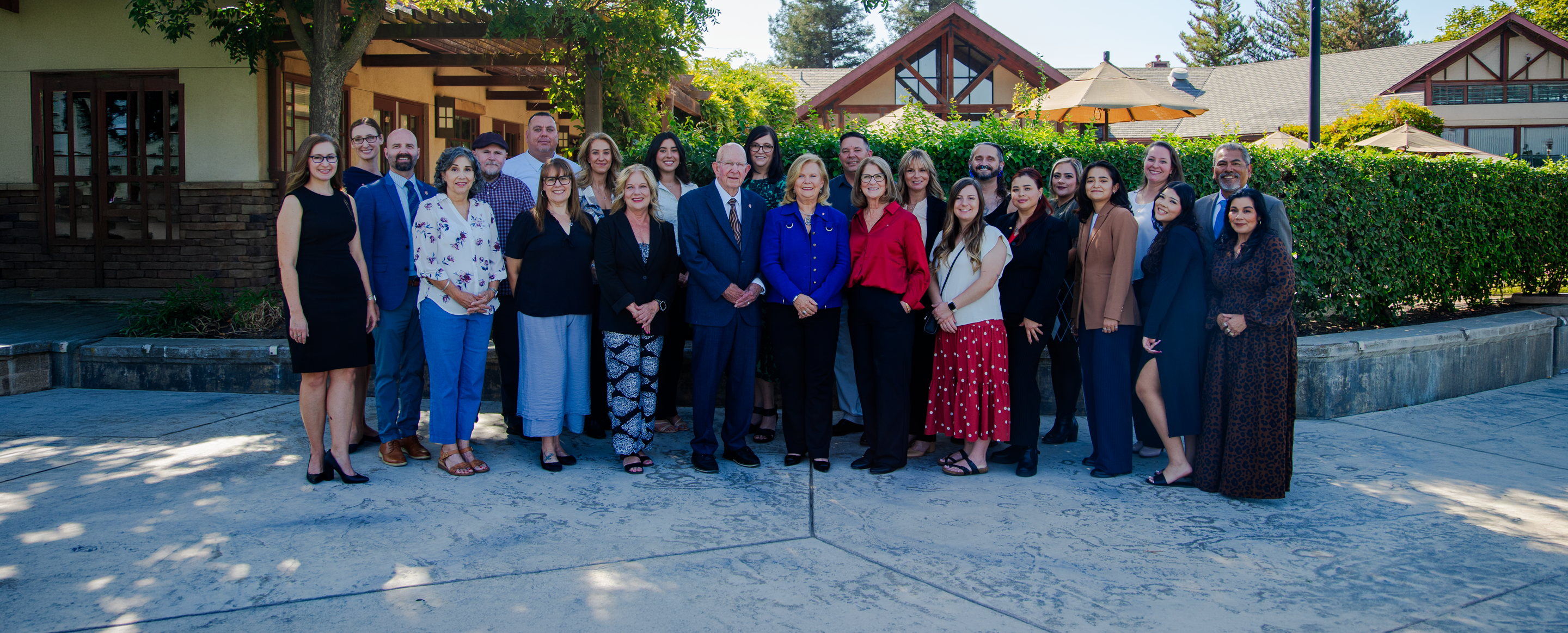 A group of 22 people poses outdoors in front of a building surrounded by trees and greenery during a Rogers Scholars event.