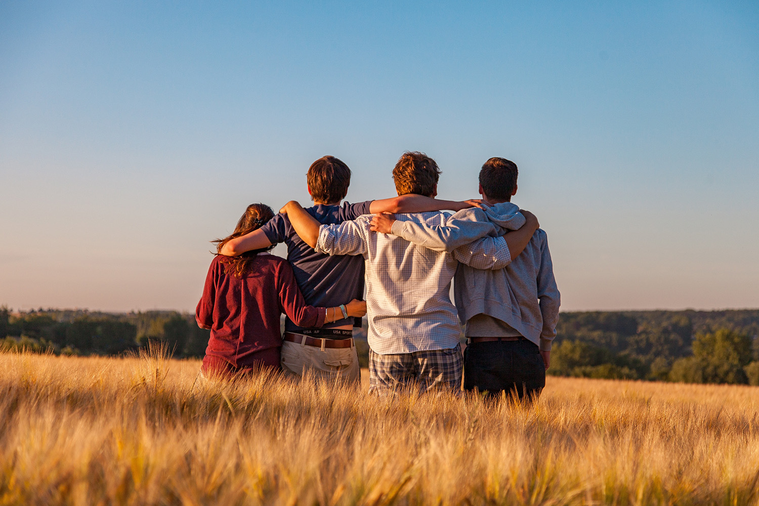 Four individuals hugging while looking off into the distance.