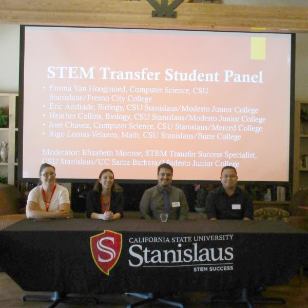 four panelists at desk in front of summit presentation 