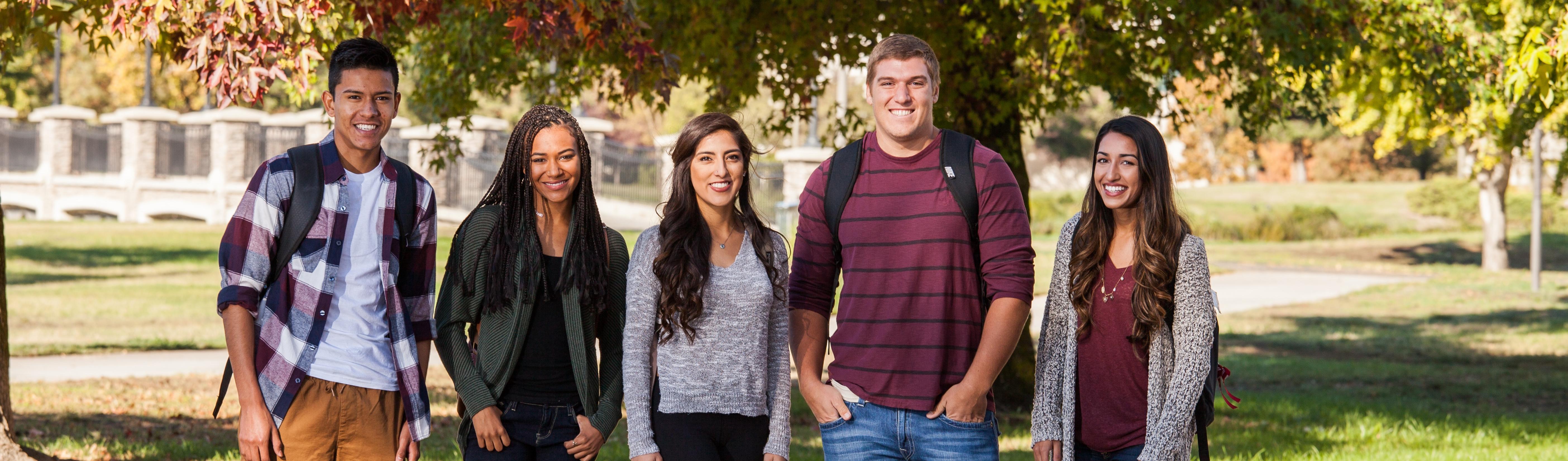 Five students smiling in front of bridge on campus