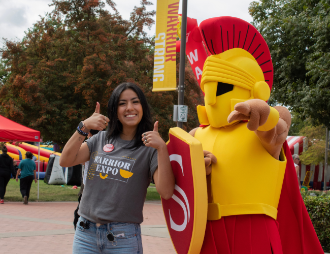 Titus and a student pose with their thumbs pointing up. 