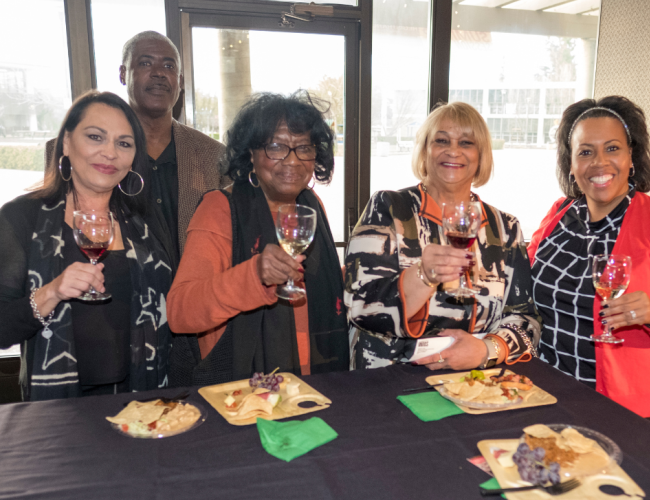 Five individuals, four women and one man, gather around a table, each holding a wine glass in a festive atmosphere.
