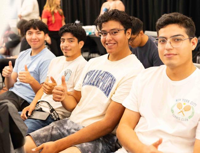 Four students in a group photo with their thumbs pointing up