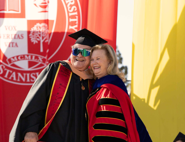 Graduate poses with President Britt Rios-Ellis at Commencement ceremony