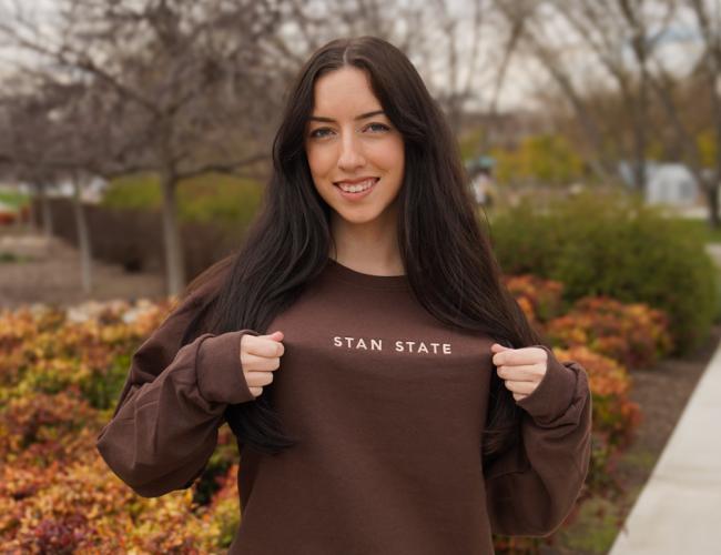 A student wearing a brown Stan State branded crew neck sweater