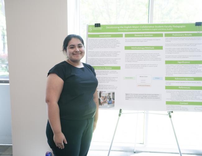A grad student poses next to a research poster