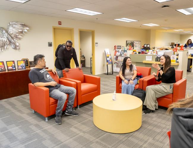 Students and staff socializing in lounge with orange chairs