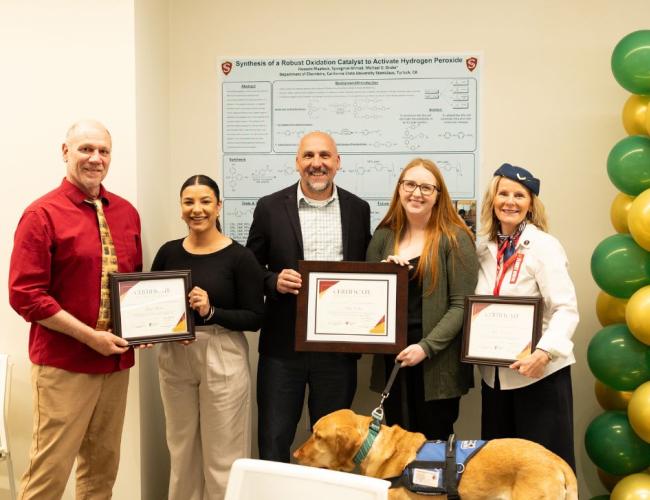 Staff in a group photo with graduate students showcasing earned certificates
