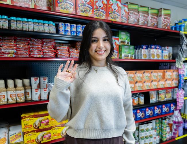 Student smiling in front of food pantry shelves