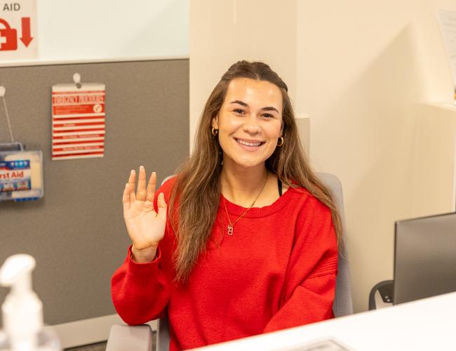 Learning commons staff member smiling and waving at front desk