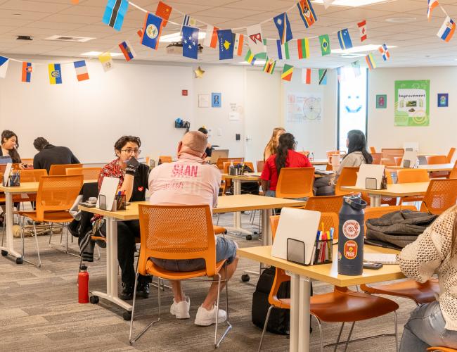 Students studying at tables with international flags on ceiling