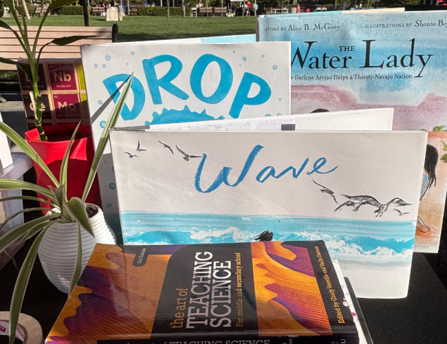 Three children's picture books behind a stack of college textbooks.