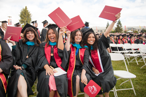 Four women graduates holding up diplomas