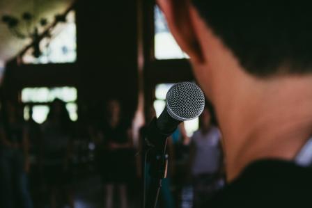 Person speaking on a mic in front of a crowd