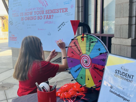 ASI member writing on a whiteboard next to a table with ASI-related activities