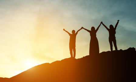 Three people holding hands on a hill, with the sun in the background