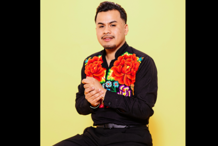 Poet yosimar reyes sitting on a stan stool. Hands together. smilling.