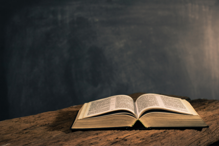 a bible on a desk with a chalk board in the background.