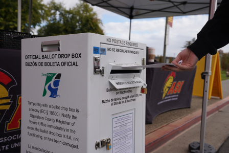 A voter slips a ballot into an official ballot box at Stanislaus State.