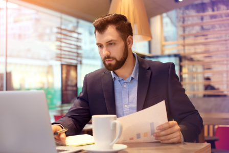 a man sitting in front of a laptop while reviewing paperwork