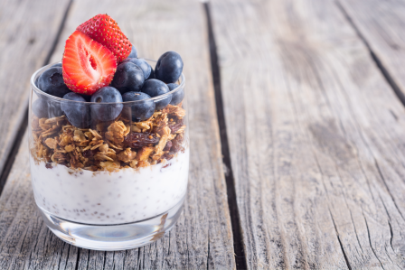 a yogurt parfait with berries in a clear glass sitting on a picnic table