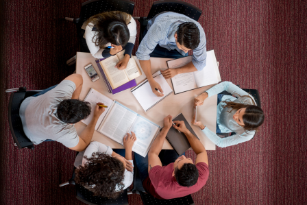 students gathered around a table studying, with books and paperwork laid across the table