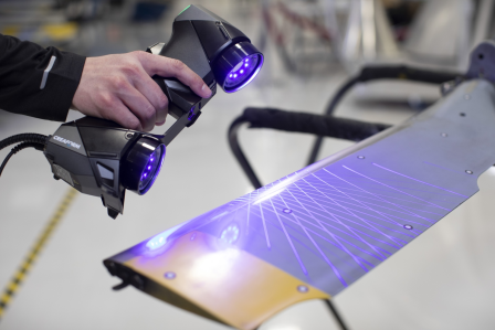 A person operates a 3D scanner, in a workshop setting.