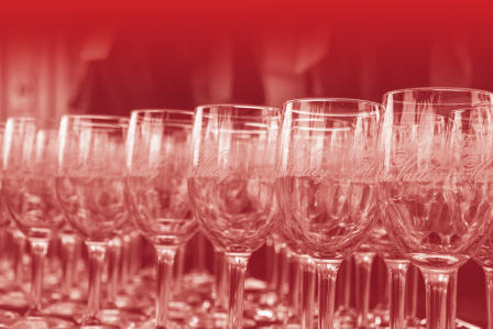 Rows of empty wine glasses with elegant script etched onto them, arranged closely together under a soft red gradient filter, creating a refined and festive atmosphere.