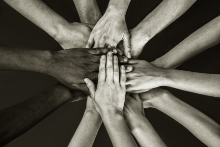 group of people from different ethnic backgrounds place hands in center.