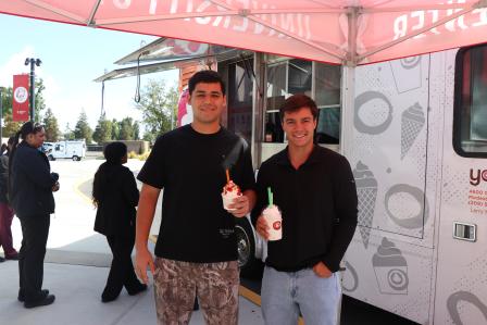 Two students holding frozen yogurt cups in front of the Yogurt Mill truck at Stan State