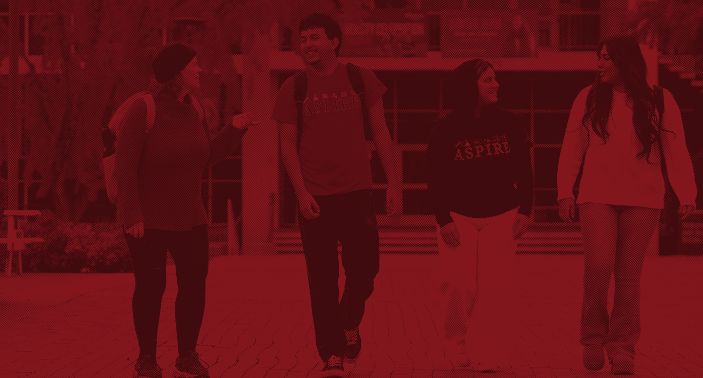 Four students walk together on a campus path, smiling and engaged in conversation. The image has a red color overlay, creating a warm, friendly tone.