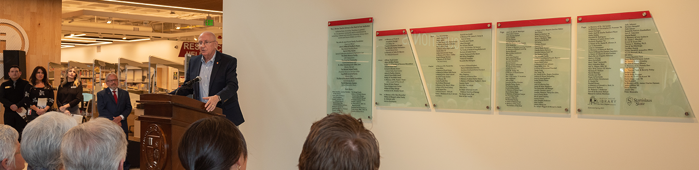 Mark Vasché speaks at the podium in front of the donor wall