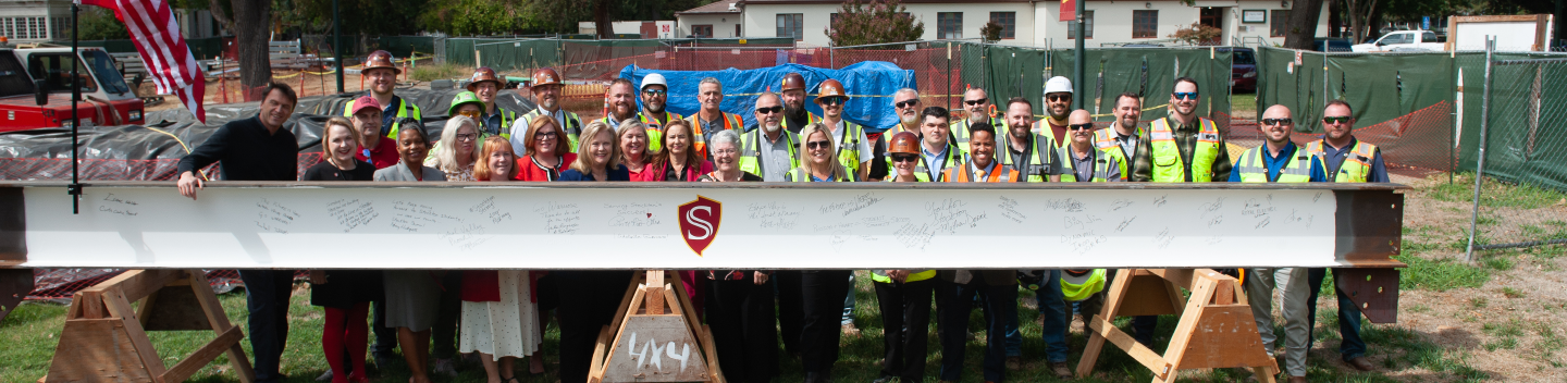 Group photo standing behind a structural building beam