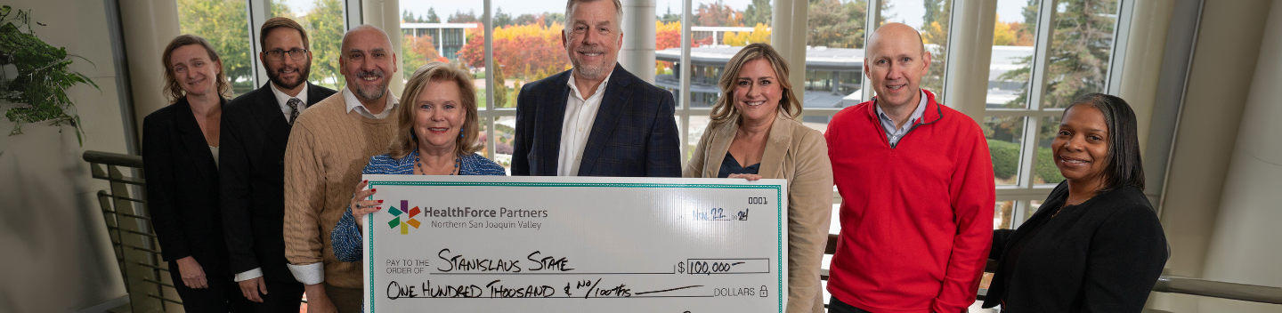A group of university leadership proudly holding the celebratory check donated by Healthforce Partners.