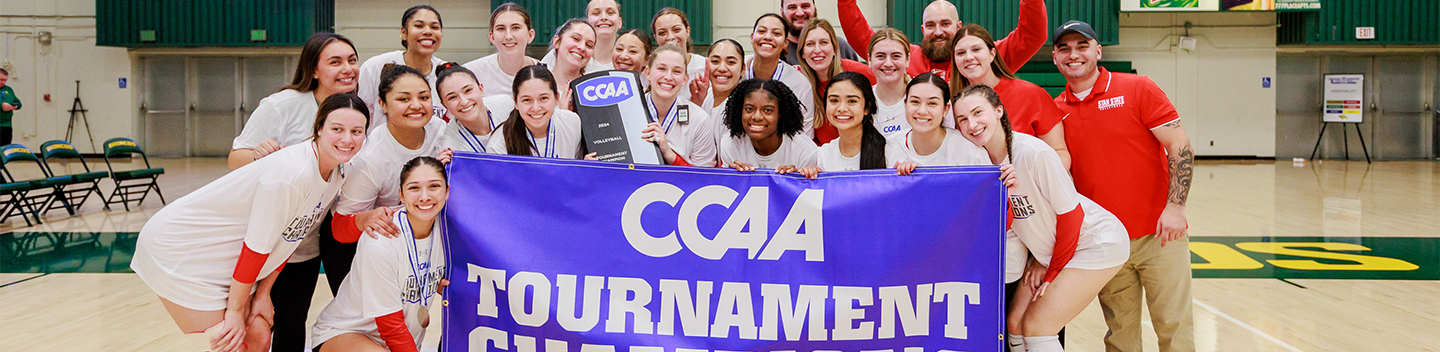 Warriors volleyball team posing with their 2024-2025 CCAA Tournament Champions banner 