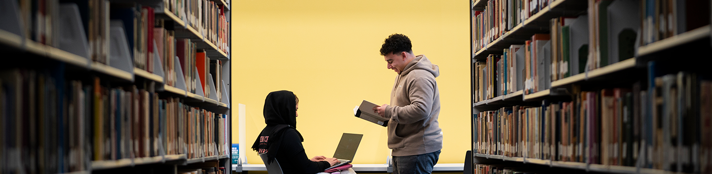 Two students studying in the library among the stacks.