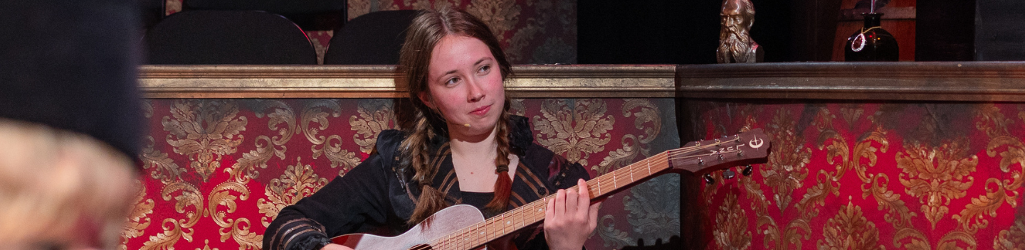An actress is seen on stage with a guitar