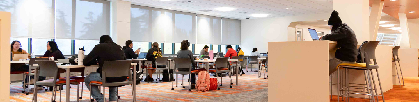 Stanislaus State students study and work at tables and individual workstations in a bright campus learning space.