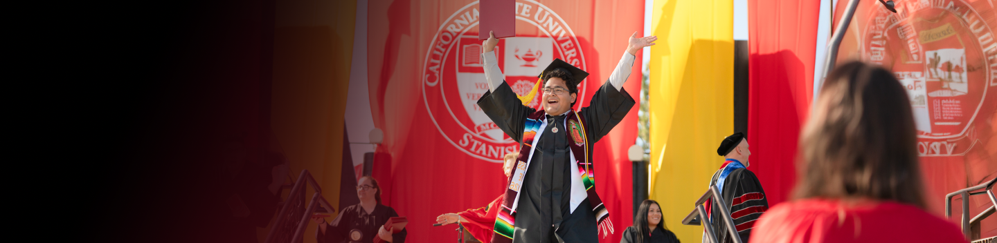 Student walking the stage at Commencement holding up their diploma
