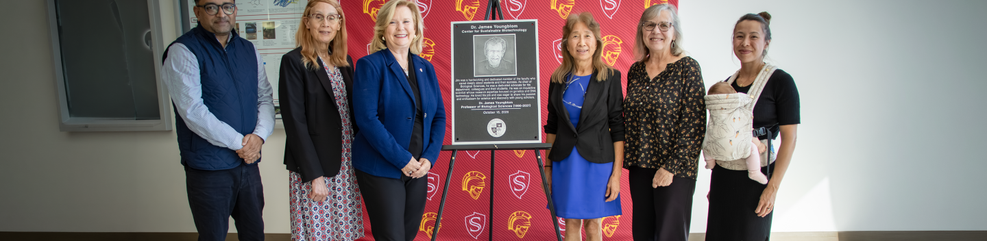 Six people pose beside a commemorative plaque honoring James Youngblom at the dedication of the Center for Sustainable Biotechnology.