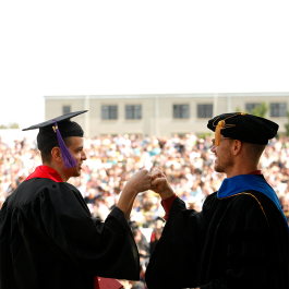 faculty member and graduating student fist bump at commencement ceremony