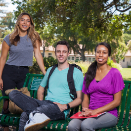Three students on a bench pose for a photo.