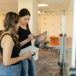 A tutor and student glance at notes in front of a whiteboard