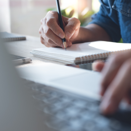 Person taking notes and looking at computer