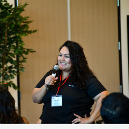 Woman speaking to an audience with a microphone.