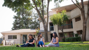 Three students converse on the lawn by Village I.