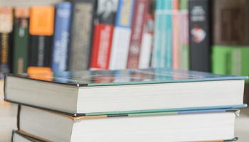three books stacked in front of bookshelf