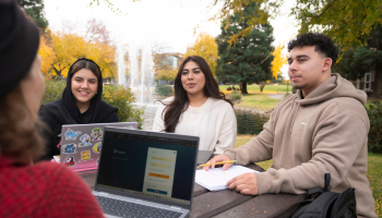 Four students chat at a table near Bizzini Hall at Stan State